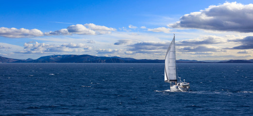 Sailboat travels with wind help, in calm sea. Cloudy sky background, banner.
