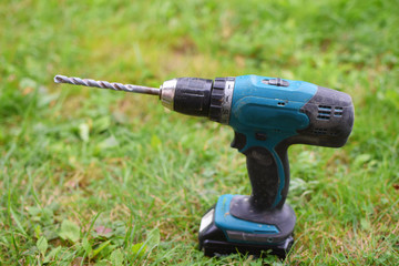 Old dirty electric cordless drill with rechargeable accumulator on green grass background with copy...