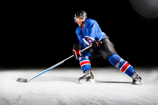 Hockey player with stick turning around skating on ice against black background