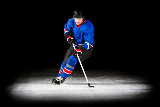 Young hockey player with stick skating on ice isolated on black background