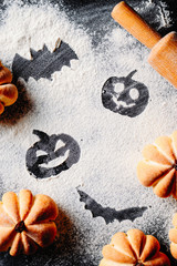 Drawing Halloween pumpkin head jack lantern and bat on wheat flour background with cakes in the shape of pumpkin, top view