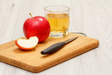 Glass of apple juice with red apple and knife on wooden cutting board