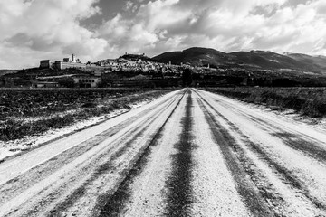 View of Assisi town (Umbria) in winter, with a field covered by snow and sky with white clouds