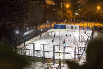 Children and adults skate at the ice rink on a winter evening