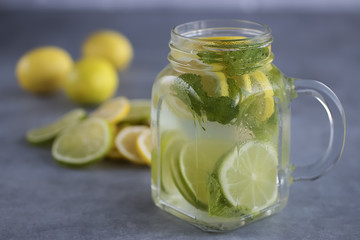 Refreshing lemonade with lemon and lime slices and mint leaves in a glass mug on a gray background.