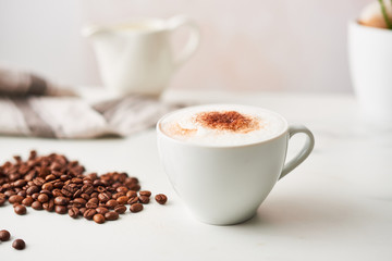 Cappuccino in a white ceramic coffee cup with roasted coffee beans. Feminine rose background with...