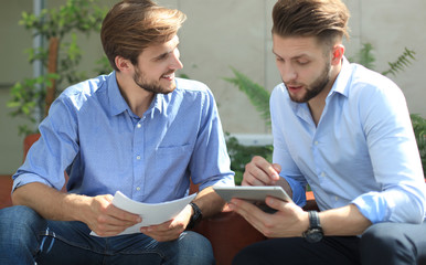 Mature businessman using a digital tablet to discuss information with a younger colleague in a modern business office.