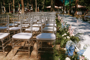 Chairs with white yarn on green grass were preparing for the outdoor wedding