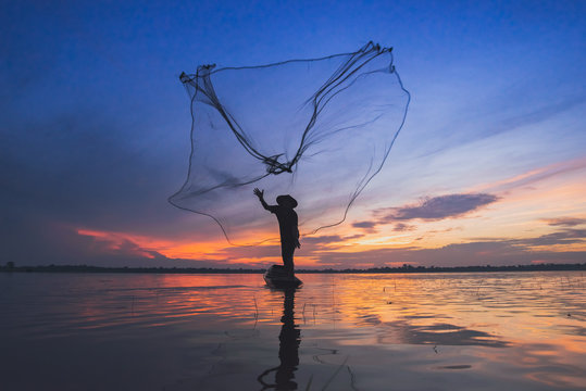 Asian fisherman on wooden boat casting a net for catching freshwater fish in nature