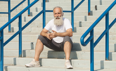 Fototapeta premium closeup grey bearded old man in white vest ready to do morning exercises drink water bottle