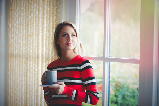 Young girl with cup of coffee stay near window at home. Autumn season