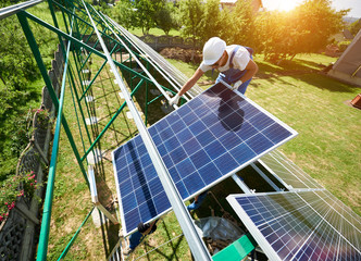 Professional worker installing solar panels on the green metal construction, using different...