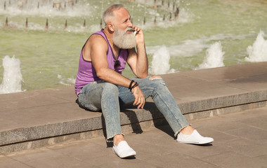 Trendy senior man using smartphone in downtown center outdoor - Mature fashion male having fun with new trends technology - Tech and joyful elderly lifestyle concept