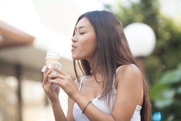 Happy young smiling asian brunette woman eating ice cream on green trees background in Park