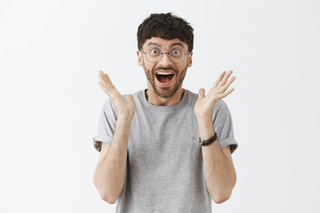 Thrilled excited and over-emotive attractive happy guy in glasses smiling broadly gasping and screaming from joy and happiness gesturing with palms clapping hands from surprise and rejoice