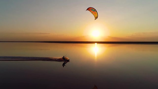 Orange sunset over a lake on which a lonely kitesurfer rushes