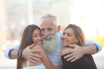 Obraz na płótnie Canvas Happy Bearded senior man hugging his young friends.