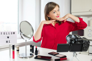 Closeup portrait of young positive European female making video for beauty blog posing in red...