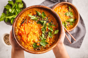 Yellow Indian vegan lentil soup curry with parsley and sesame in a wooden bowl in hands.