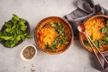 Yellow Indian vegan lentil soup curry with parsley and sesame in a wooden bowl.