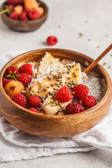 Oatmeal porridge with chia seeds, berries, peanut butter and hemp seeds in wooden bowl, white background.