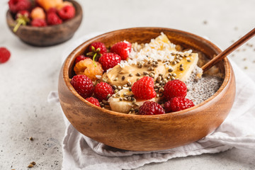 Oatmeal porridge with chia seeds, berries, peanut butter and hemp seeds in wooden bowl, white background.