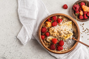 Oatmeal porridge with chia seeds, berries, peanut butter and hemp seeds in wooden bowl, white background.