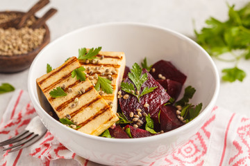 Baked beet salad with grilled tofu parsley and oil in a white bowl.
