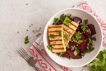 Baked beet salad with grilled tofu parsley and oil in a white bowl, top view, copy space.