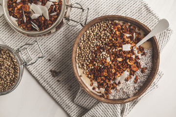 Smoothie bowl with granola, chia pudding and hemp seeds in coconut shell bowl.