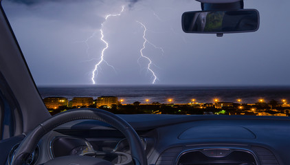 Car windshield with view of lightning storm over the sea