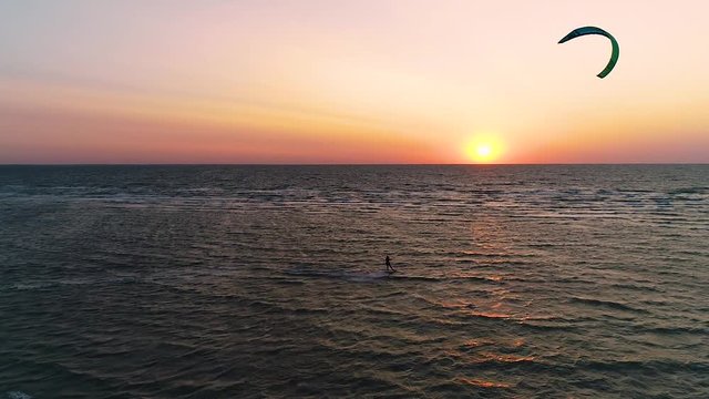 Tricks on Kitesurf. Orange sunset in the sea, a couple of people engaged in kitesurfing. Aerial shooting