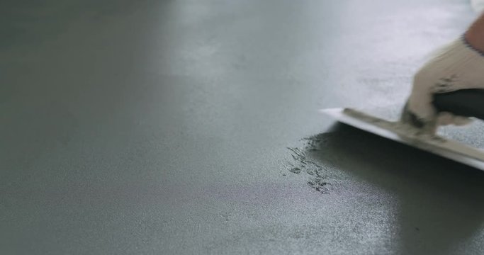 Slow motion closeup male worker applying micro concrete plaster coating on the floor with a trowel