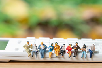 Miniature people sitting on white calculator using as background business concept and teamwork...