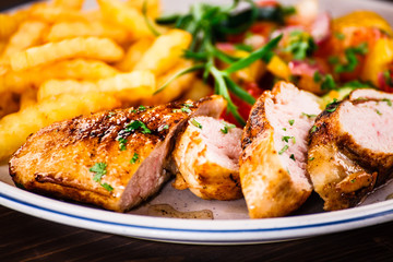 Grilled chicken fillet with french fries on wooden background
