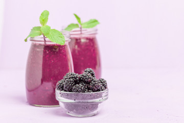 Blackberry smoothie - raw organic drink with fresh ripe forest berries on pastel violet background.