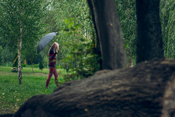 Obraz premium creative foreshortening between trees of lonely teenager girl walk in autumn park natural place under umbrella in wet rainy gray day time 