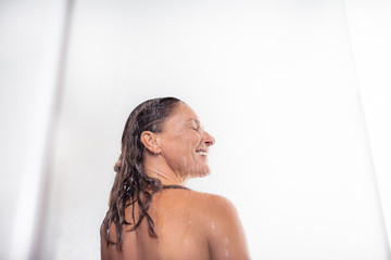 Fototapeta na wymiar Relaxing after work. Back view portrait of beautiful middle aged lady standing under water drops and smiling
