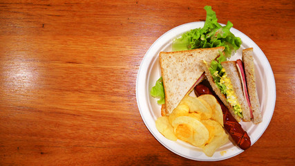 Breakfast at the restaurant. Sandwich, Sandwich, sausage and potato chips in the white paper plate.