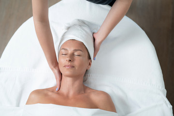 Fototapeta na wymiar I feel so good. Top view portrait of happy woman with closed eyes lying on massage table during skincare procedure. Masseuse arms touching client neck