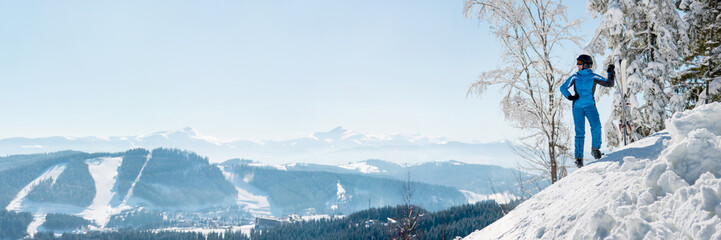 Panoramic shot of a female skier resting on top of the mountain observing nature at ski resort on a...