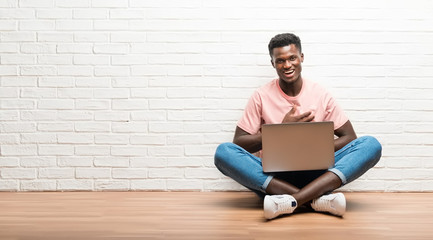 Afro american man sitting on the floor with his laptop laughing