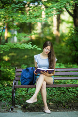 Obraz premium Young woman with a notebook in hands sitting on a park bench