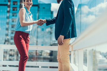 Cheerful girl shaking hand of businessman while speaking with him outside. Happy businesswoman communicating with male concept