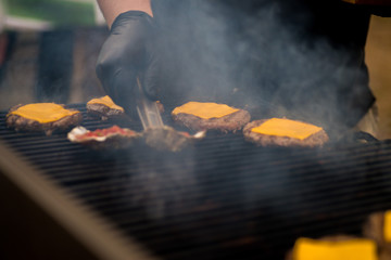 cook in gloves is cooking a cutlet with cheese for burgers on an open fire - obrazy, fototapety, plakaty