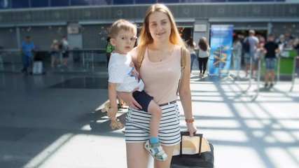 Slow mtoion video of beautiful smiling woman holding her toddler boy and walking ininternational airport terminal - Powered by Adobe