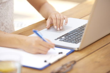 Fototapeta na wymiar Close-up of woman typing on laptop and writing something