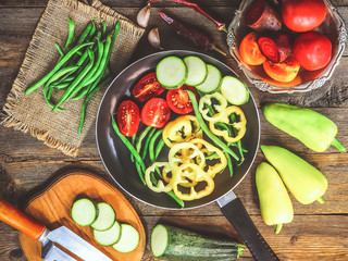 sliced vegetables. tomatoes, peppers, pods beans in a frying pan. wooden background.