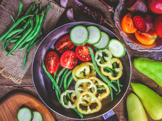 sliced vegetables. tomatoes, peppers, pods beans in a frying pan. wooden background.