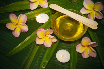 Sugaring Hair Removal Set with Sugar Paste and Spatula on Beautiful Background with Frangipani Flowers and Palm Tree Leaves with Candles in Spa Salon